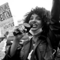 Woman in demonstration with a megaphone in hand and protest posters around her